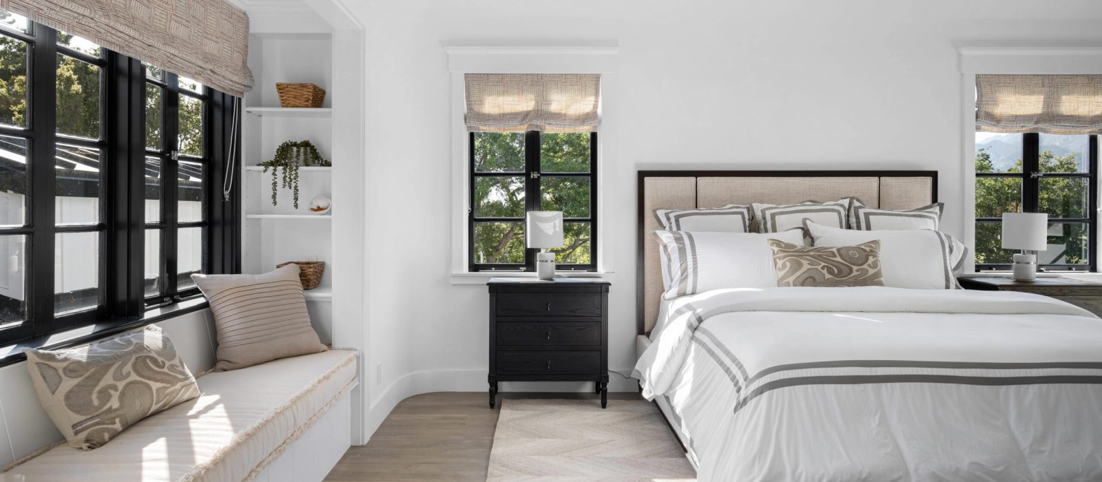 A cozy bedroom interior featuring a double bed situated in front of a large window, next to a comfy armchair